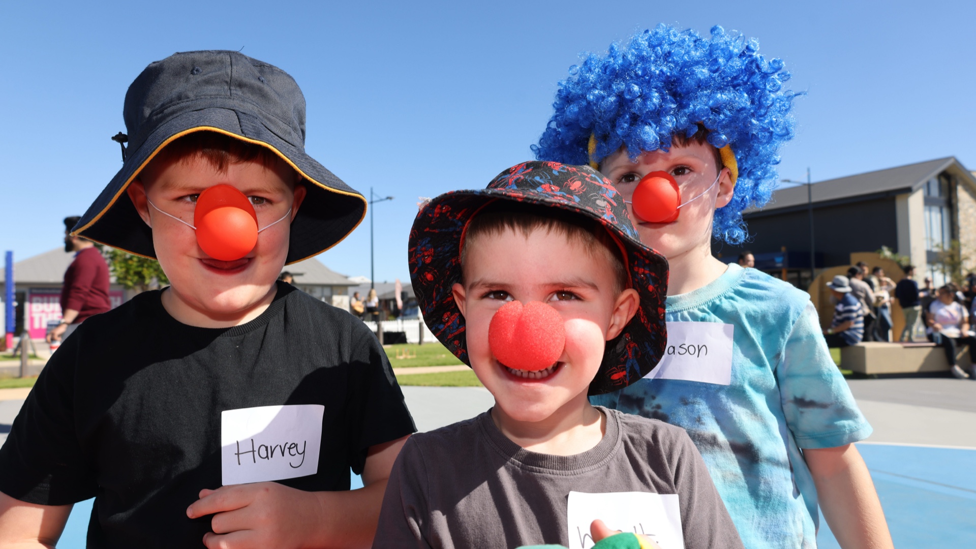 Three young boys posing for a photo with red balls on their noses