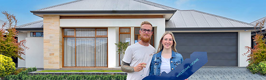 A young couple standing infront of their new home at Riverlea, holding a sign in the shape of a key that reads welcome home