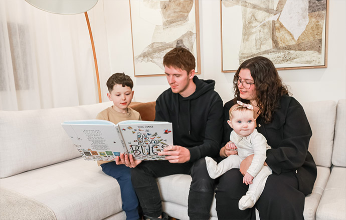 A mother and father sitting on the couch reading a children's book to their son.