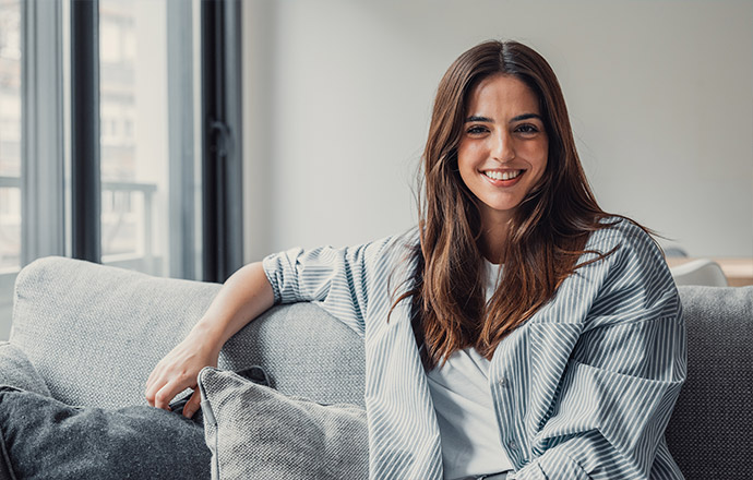 A woman sitting on a couch inside her home at Riverlea, smiling.