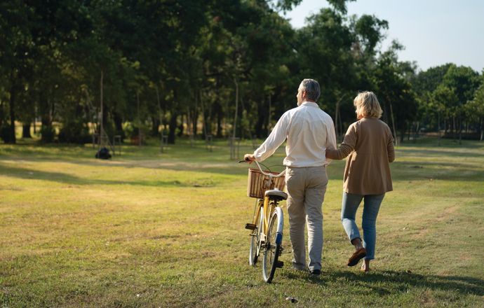 A couple walking through parklands with a bicycle