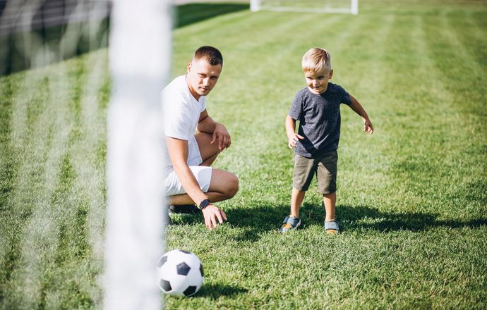 A father and child playing soccer together