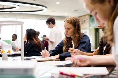 Several school students sitting in a classroom writing in notebooks.