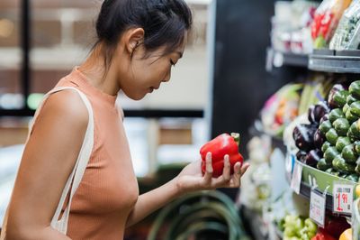 A young person inspecting a capsicum in a supermarket.