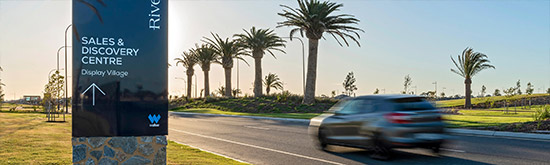 A car driving along the palm tree lined roads towards the Sales Centre.