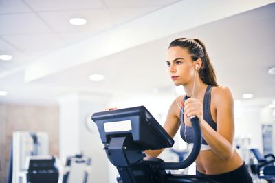 A young person wearing activewear working out on an exercise machine with headphones in.