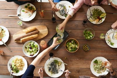 A group of people sharing a meal around a large wooden table one of the people pours water into another’s glass