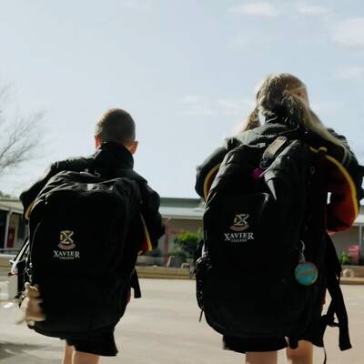 Two schoolchildren with Xavier College backpacks walking through the schoolyard.